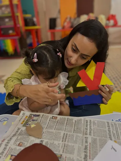 A mother guides her daughter's hands as they assemble a colorful paper craft, a simple yet effective way to practice fine motor control.