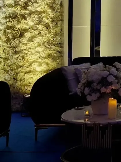 A lounge area set against the floral wall, combining a modern black sofa with soft candlelight for a chic and inviting look.