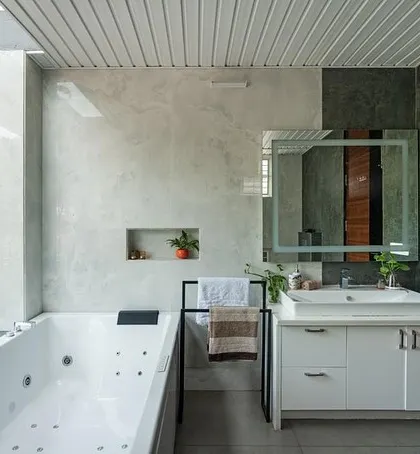 The master bathroom is designed as a luxurious space with a jacuzzi tub that overlooks the lush exterior greenery through a large window. The monochromatic color scheme adds a touch of modern sophistication.