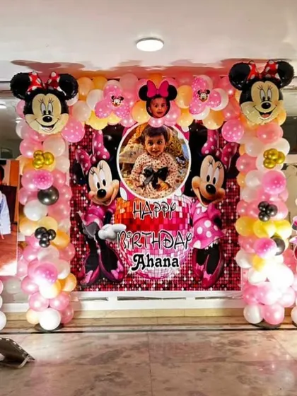 A grand Minnie Mouse themed birthday party. The decoration includes a large backdrop with custom photos, balloon pillars, and multiple Minnie Mouse character cutouts and foil balloons.