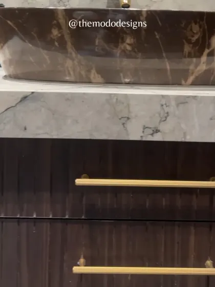 A close-up of a bathroom vanity, showcasing the beautiful contrast between a dark marble basin, a light marble countertop, and fluted wood cabinetry with sleek brass handles.