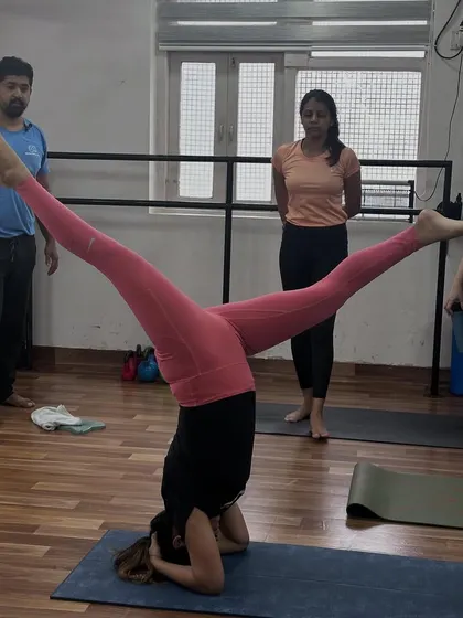 A student performs Upavistha Konasana (Wide-Angled Seated Forward Bend) in a headstand, a challenging variation requiring core strength and balance.