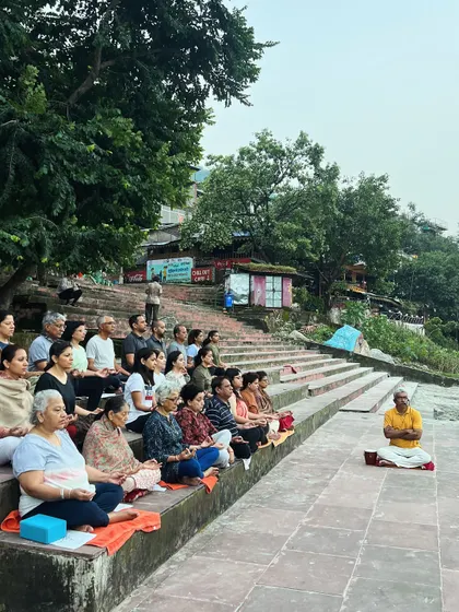 A large group practices guided meditation on the steps of a ghat in Rishikesh. Practicing together in such a powerful natural setting deepens the experience for everyone involved.