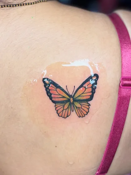 A small, colorful butterfly tattoo on the shoulder. Even small pieces can have a big impact with the right colors and placement.