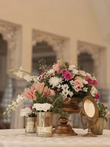 A simple yet elegant centerpiece for the lunch tables, featuring a mix of pastel flowers in a golden vase, accompanied by a small vintage-style mirror.