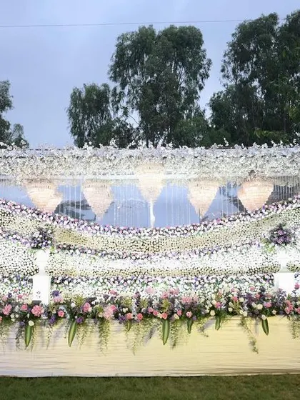 A massive floral wall for a reception, created with waves of white and lavender flowers, with crystal chandeliers adding a touch of grandeur.