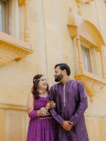 A happy, candid moment during a shoot at a palace hotel in Jaisalmer. The couple's coordinated purple outfits look stunning against the golden sandstone architecture.