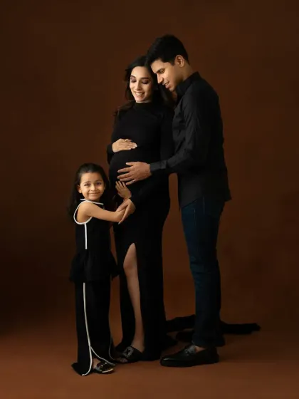 A beautiful family portrait with an expecting mother, father, and their daughter, all dressed in elegant black. This studio maternity photoshoot celebrates the growing family and the excitement of a new arrival.