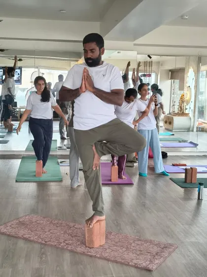 A male student demonstrates focus and stability in Vrikshasana on a block. Our TTC is inclusive and welcomes practitioners from all backgrounds to deepen their practice.