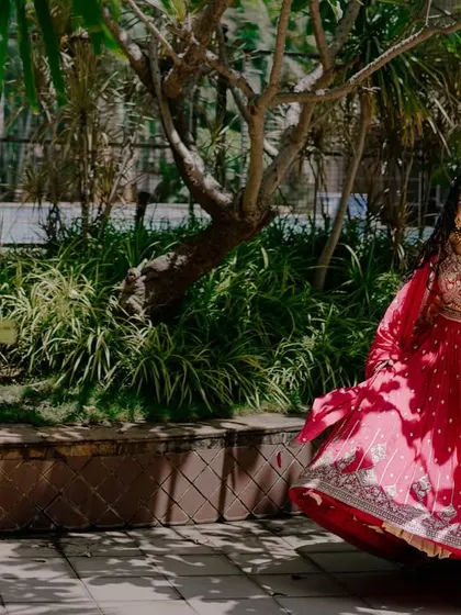 The bride twirls in her vibrant red lehenga in a beautiful garden setting. Her joyful expression and the motion of her dress create a lively and stunning bridal portrait.