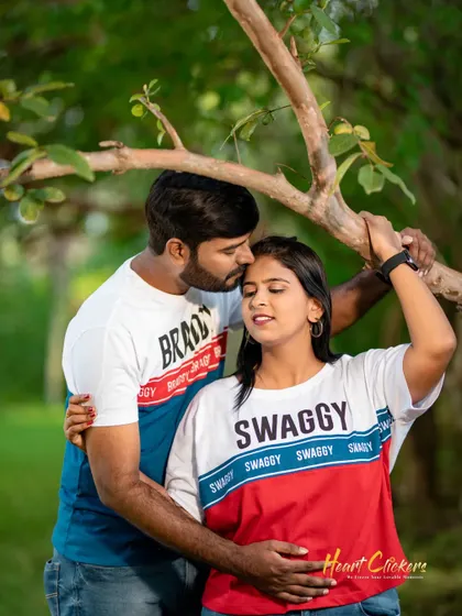 A tender pre-wedding moment in a park. The groom's gentle kiss on the forehead shows a sweet and caring connection.