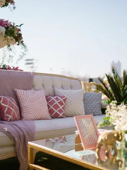 A chic lounge setup with a pastel pink and grey color scheme. The comfortable sofa is adorned with patterned cushions and a soft throw, creating an inviting space for guests to relax.