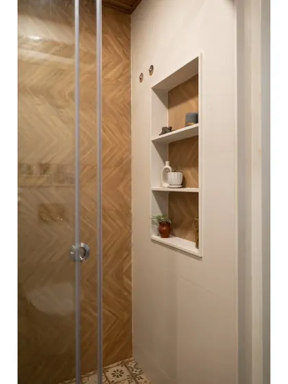 A detail from another renovated bathroom, showing a herringbone pattern wooden tile in the shower area and a built-in niche for storage, maximizing functionality in a compact space.