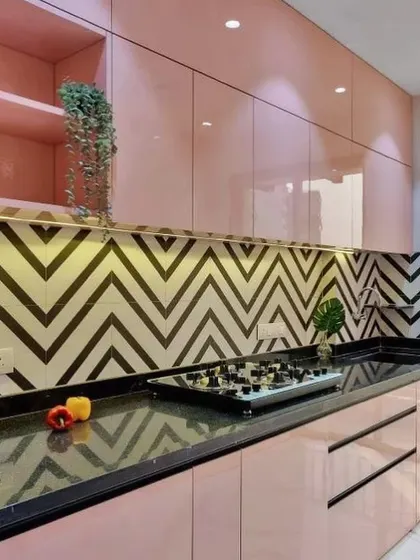 This pink kitchen makes a statement with a bold black-and-white chevron tile backsplash. The glossy pink handle-less cabinets are paired with a black granite countertop for a dramatic, high-contrast design.