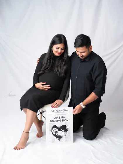 A creative announcement. The couple holds a "Newborn Times" newspaper prop that reads "Our Baby Is Coming Soon," a fun way to share the news.