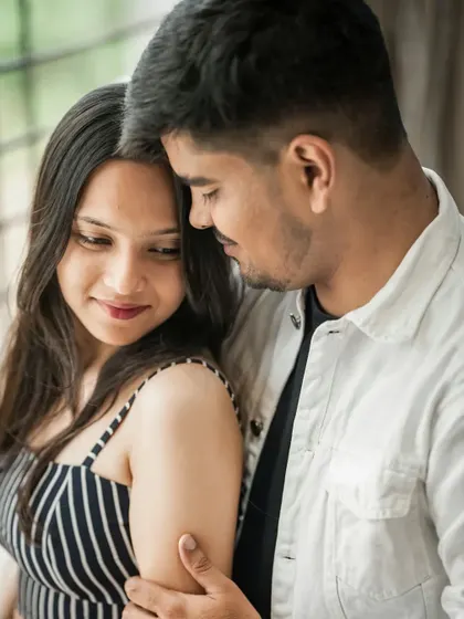 An intimate indoor pre-wedding photo, capturing a quiet moment of affection between the couple by a window.