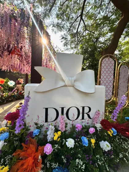 The sun shines through the hanging flowers, illuminating the Dior perfume bottle installation and creating a magical, sun-drenched effect.