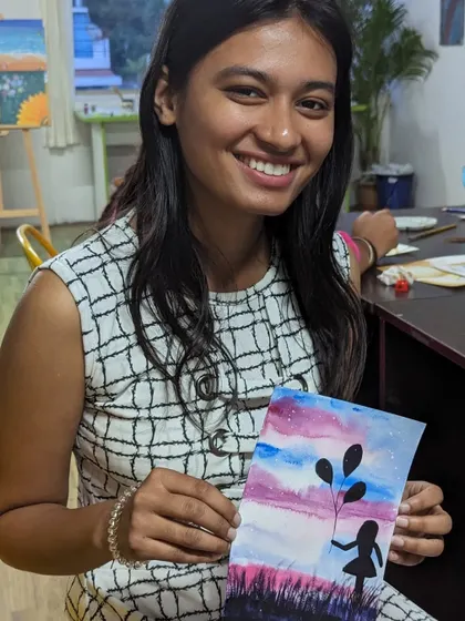 A participant with her beautiful watercolor painting of a girl holding balloons against a sunset sky.