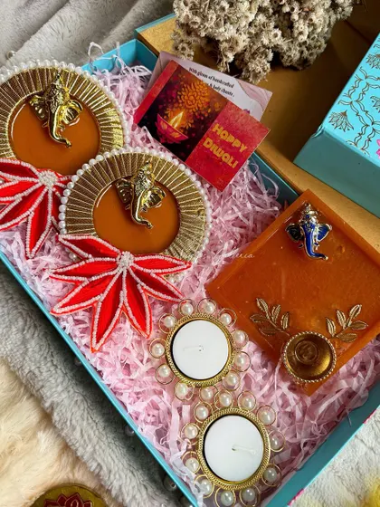 An orange-themed Diwali hamper featuring Ganesha hangings, a matching platter, and pearl-accented diyas.