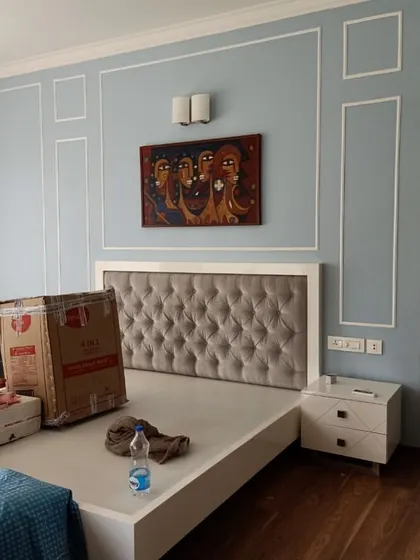 An elegant bedroom featuring a tufted grey headboard against a powder blue wall with decorative molding. This image, taken during setup, shows how we blend classic elements with modern furniture.
