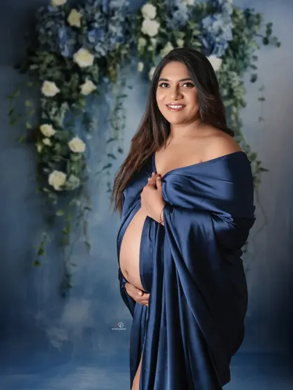 A joyful portrait capturing the beautiful glow of pregnancy. The combination of the blue satin gown and the floral backdrop creates a serene and classic maternity look.