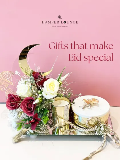 A mirrored tray serves as the base for this elegant Eid hamper. It features a scented candle, a gift box, and a beautiful floral arrangement with a golden crescent moon. The reflective surface adds a touch of glamour to the entire presentation.