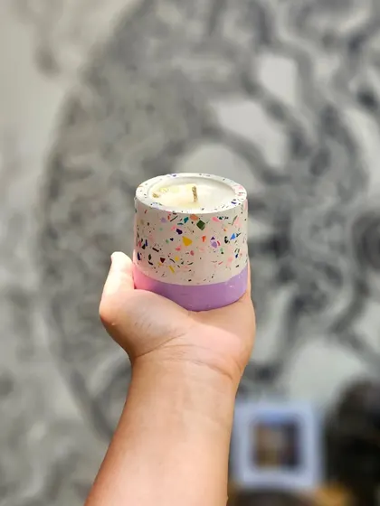 Holding up a terrazzo candle with a lavender base. The combination of the playful terrazzo pattern with a solid color block is a popular customization option.