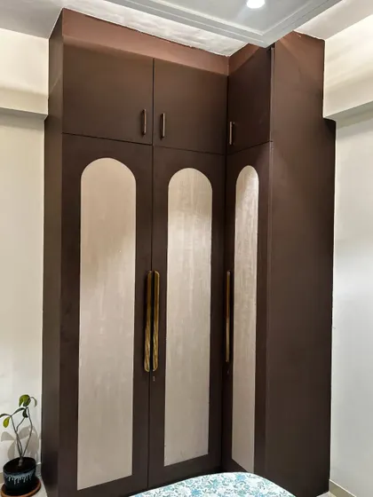 This is a custom-designed corner wardrobe in a dark wood finish with contrasting cream-colored arched panels. It’s a great example of how we can tailor furniture to fit unusual corners and maximize storage.