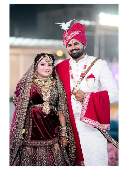 A classic wedding portrait of the couple, looking proudly at the camera. Their coordinated red and white outfits look stunning and traditional.