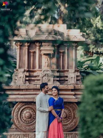 A classic couple portrait in vibrant traditional outfits, perfectly framed by the intricate details of a stone chariot replica.