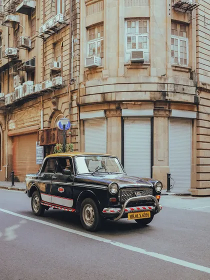 The iconic 'kaali-peeli' Premier Padmini taxi in motion. This shot captures a piece of Mumbai's identity against the backdrop of its beautiful old buildings.