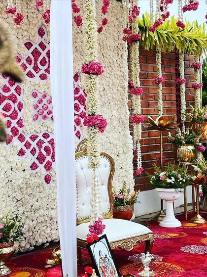 A close-up of the Seemantham stage, showing the intricate floral backdrop made of white and pink flowers, and the elegant throne-style chair for the mother-to-be.