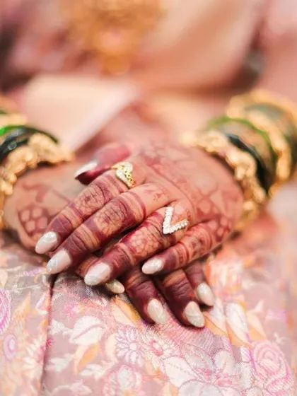 A quiet, elegant shot of the client's hands, showing the beautiful contrast between the dark henna, the light nails, and the traditional bangles.
