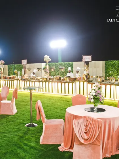 A beautiful outdoor catering setup on a lush green lawn. The blush pink table linens and floral arrangements add a soft, romantic touch perfect for weddings and receptions.