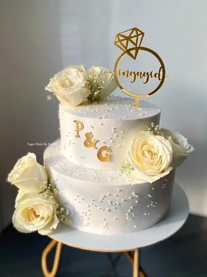 An elegant two-tier engagement cake with a custom topper and beautiful white roses. The simple pearl details add a touch of class to this special occasion cake.