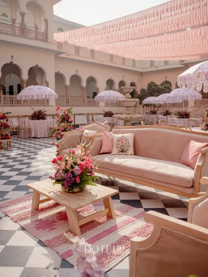 A lounge area from the Jaipur brunch, with a plush pink sofa, a rustic wooden coffee table, and a patterned rug. This creates a comfortable and stylish space for guests to relax.