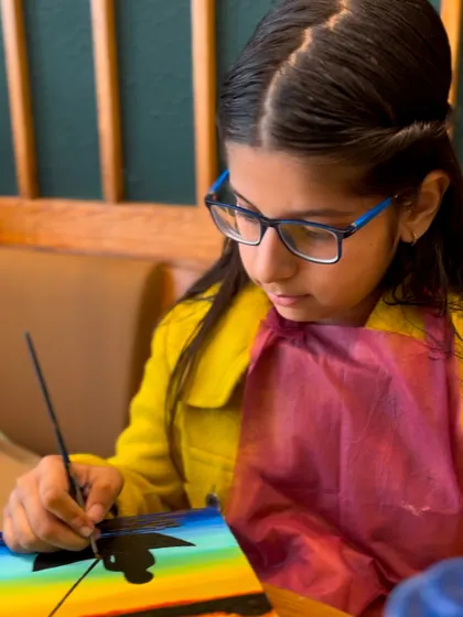 A young artist deeply focused on her sunset painting.