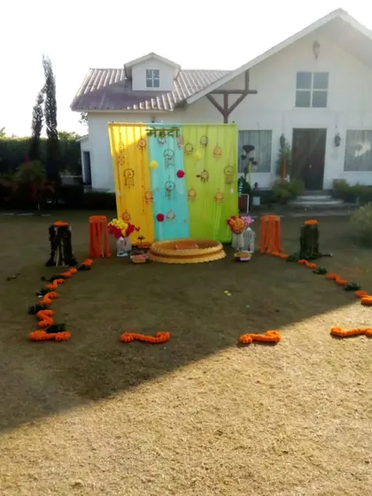 A simple outdoor Mehendi setup in a lawn, featuring a colorful backdrop and a central 'urli' for rituals.