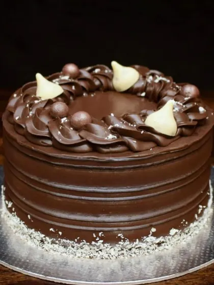 A rich and decadent chocolate truffle cake. This design features a textured ganache finish, a piped chocolate wreath on top, and is decorated with Hershey's Kisses and chocolate pearls.
