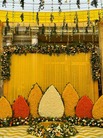 Another angle of the traditional Haldi backdrop, highlighting the hanging green foliage and the beautiful floral border at the top.
