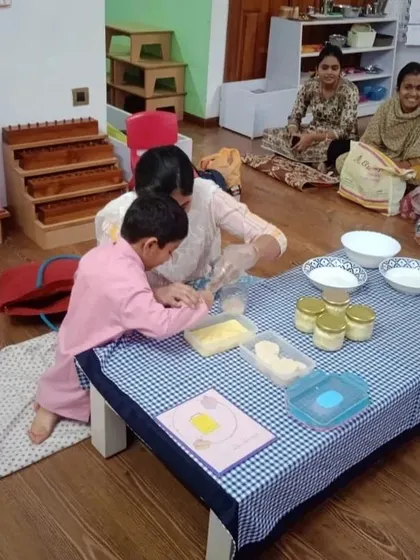 A child gets hands-on with making butter, with parents observing in the background. We encourage parent involvement, creating a strong community bond between home and school.