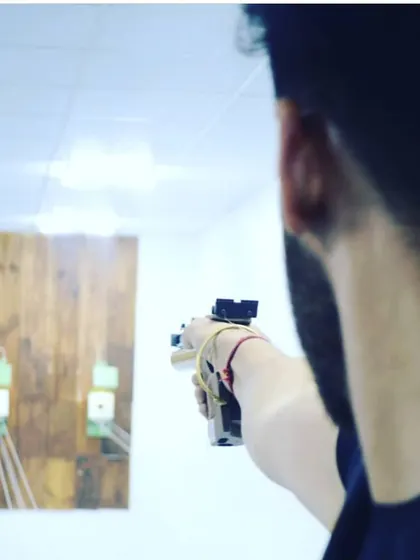 An over-the-shoulder perspective of a shooter aiming his pistol at the target, showcasing the focus required for this precision sport.