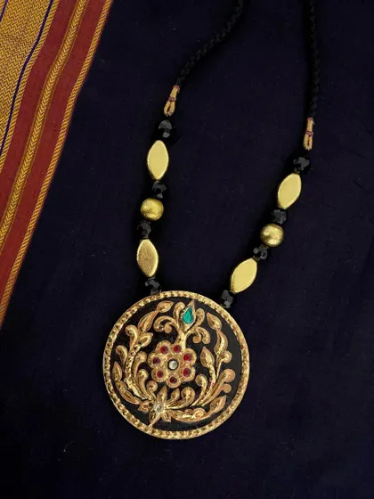 Another view of the black and gold floral Tanjore pendant, styled against a traditional silk cloth to highlight its ethnic charm.