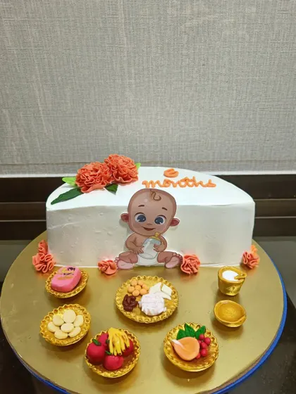 A unique cake celebrating a baby's "Annaprashan" or first solid food ceremony. The design features miniature edible versions of traditional foods served during the ritual.