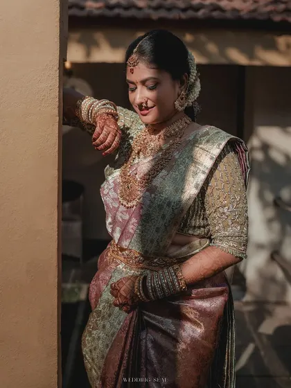 The bride in a moment of quiet contemplation, bathed in warm, natural light. Her iridescent saree and serene expression create a portrait of pure elegance.