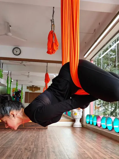 A student gracefully holds an inverted pose, demonstrating the core strength and trust developed through our aerial yoga practice.