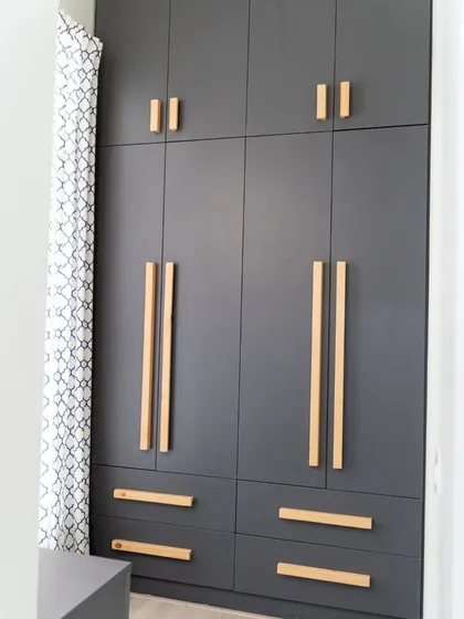A walk-in wardrobe in a dark grey finish with contrasting natural wood handles. The design is modern and spacious, with a mix of drawers and cabinets for organized storage.