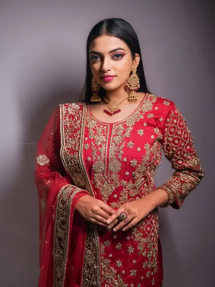 A stunning portrait in a heavily embroidered red bridal outfit. The studio lighting is crafted to make the gold threadwork pop.