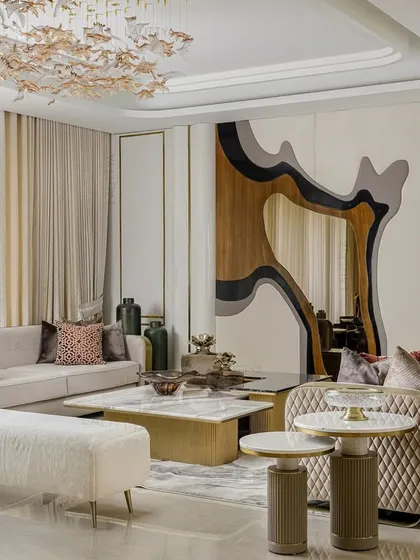 A wider view of the living area, showing how the sculptural wall mirror reflects the custom chandelier and adds depth to the room. The arrangement of the sofas and bench creates a welcoming and functional seating group.