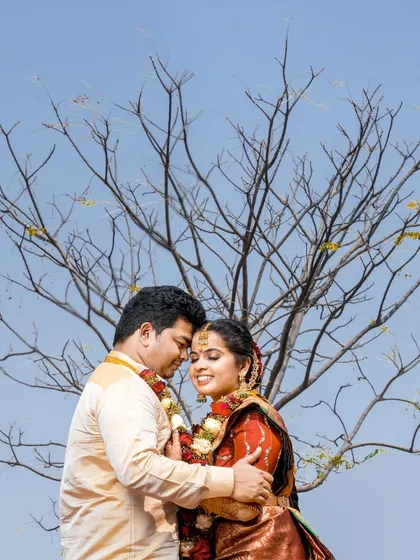A romantic embrace against a clear blue sky, using the bare tree branches to create an interesting visual frame.